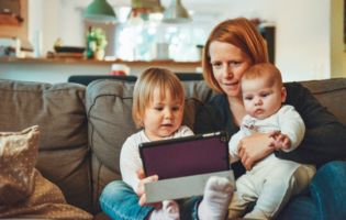 Mother with Two Children Sitting on a Couch and Looking at a Tablet