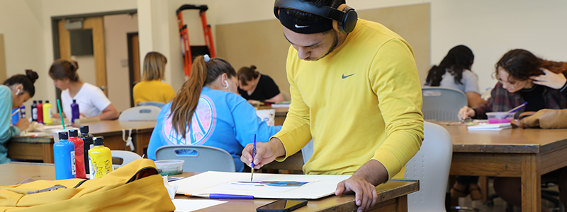 Male student drawing on paper on a table.