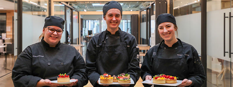 Three female culinary students holdings plates of tarts