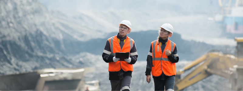 Two People in Construction Outfits Walking Around a Site in the Mountains